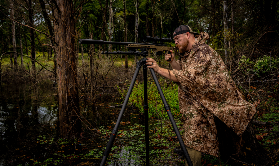 Hunter setting up a rifle on a KJI shooting tripod in wet uneven terrain