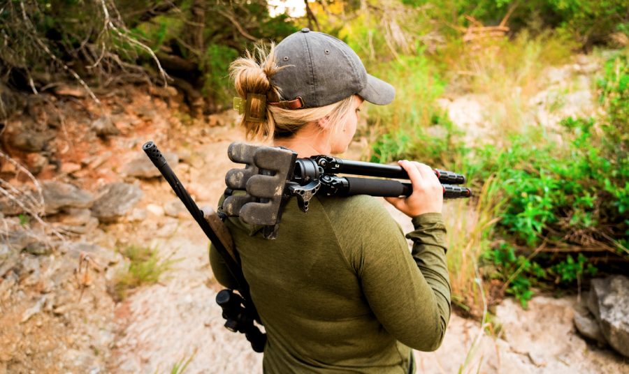 Hunter carrying a folded KJI tripod over her shoulder on rocky terrain